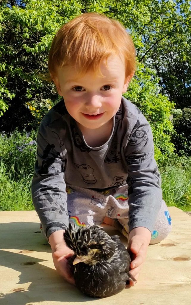 Young boy holding a chicken smiling outdoors